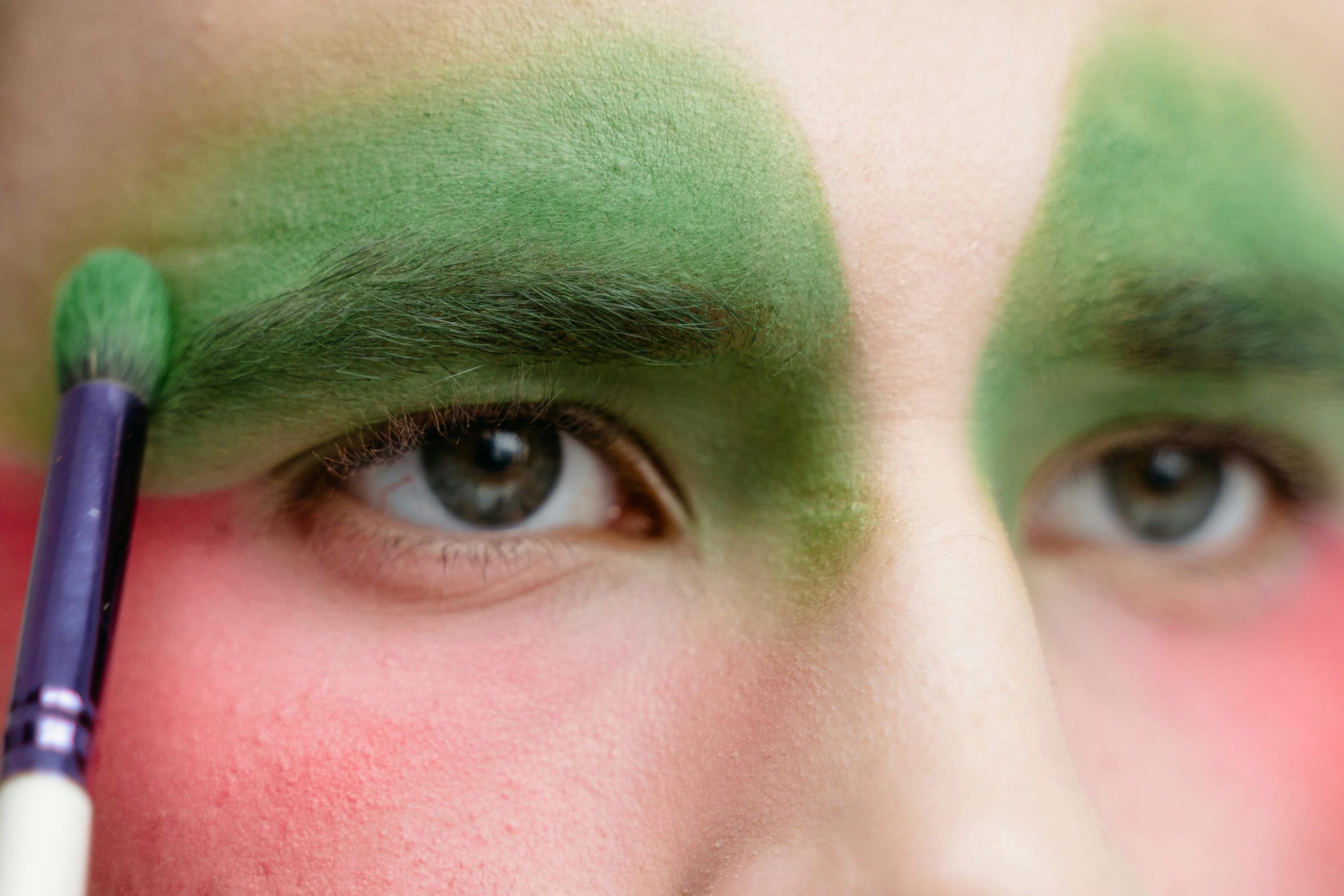 Close-up shot of fingers applying glittery green eyeshadow around the eyes