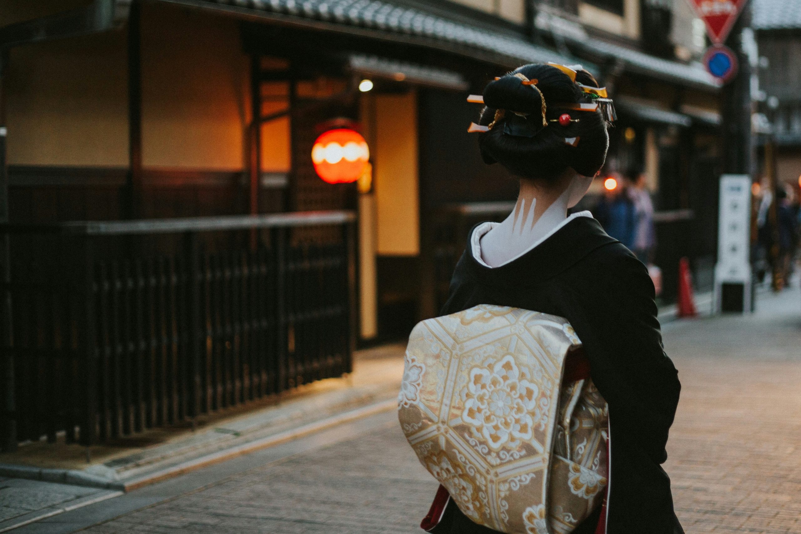 Woman dressed realistically as an elderly person holding cane beside pumpkin lantern
