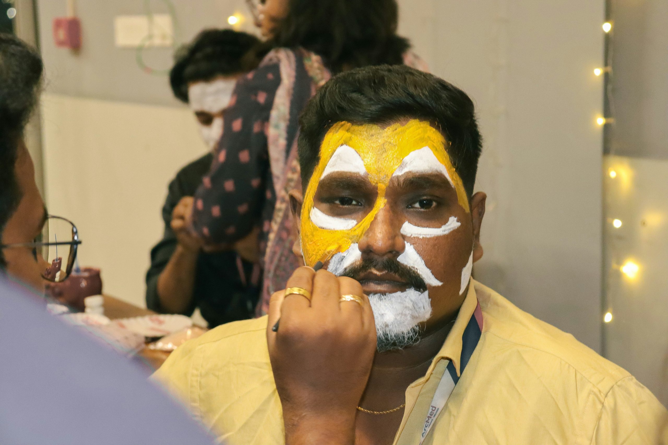 A model mid-transformation with bright blue face paint and glittery eyes illustrating a halloween-themed stage makeup style.