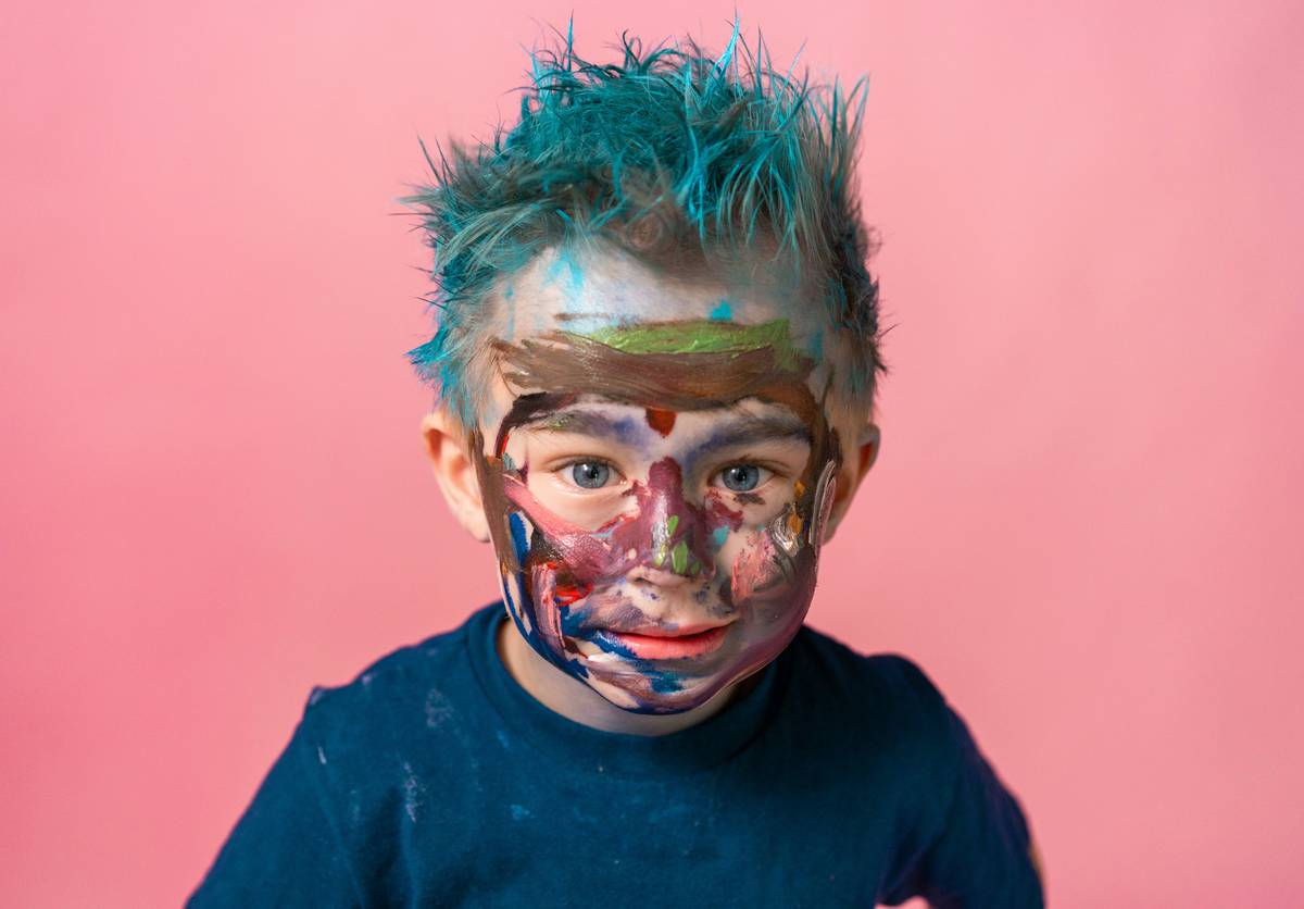A child smiling with colorful pumpkin-themed face paint applied safely and neatly.